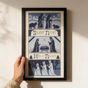 Può includere: Un ricamo a punto croce incorniciato che raffigura una scena della natività in tonalità blu navy e azzurro su sfondo crema. Il design include il testo Silent Night e Holy Night, con figure, animali e stelle disposti in una griglia.