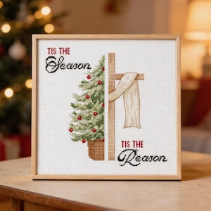 May include: A square framed cross-stitch embroidery featuring a split design. The left side shows a green Christmas tree with red ornaments in a brown pot. The right side shows a wooden cross draped with a white cloth. Text reads Tis the Season.