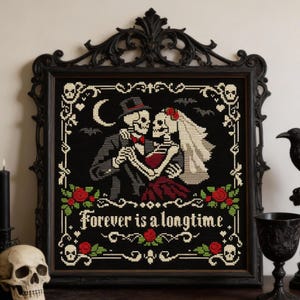 Puede incluir: Arte de punto de cruz enmarcado en negro con una pareja de esqueletos bailando, con el texto "Forever is a longtime". La obra incluye una luna, murciélagos, rosas y calaveras. El marco es ornamentado y oscuro.