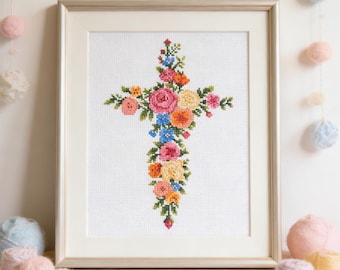 May include: Framed cross-stitch art featuring a floral cross design. The cross is adorned with colorful flowers in shades of pink, orange, yellow, and blue, set against a white background. The artwork is framed in a gold-colored frame.