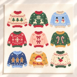 Peut inclure: Un motif de point de croix sur toile Aida blanche représentant neuf pulls de Noël. Les motifs incluent des sapins, des rennes, des bonhommes de neige, des flocons, des nœuds, des sucres d'orge, des bonshommes en pain d'épice, un Père Noël avec le texte Ho Ho Ho et du houx.