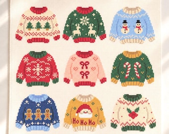 以下が含まれることがあります： 白いアイーダ布に9種類のクリスマスセーターが刺繍されたクロスステッチパターン。ツリー、トナカイ、雪だるま、雪の結晶、リボン、キャンディケイン、ジンジャーブレッドマン、Ho Ho Hoの文字が入ったサンタの顔、ヒイラギのモチーフがデザインされています。