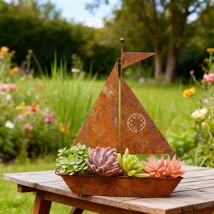 May include: A rustic metal sailboat planter with a weathered, orange-brown finish. The boat holds a variety of succulents in shades of green, pink, and orange. The planter sits on a wooden table in a garden setting.