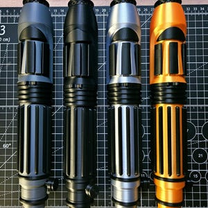 May include: Four cylindrical handles with ribbed textures and black accents, arranged vertically. The handles are coloured matte grey, solid black, metallic silver, and bright orange. Each features a circular top cap and a small side knob.