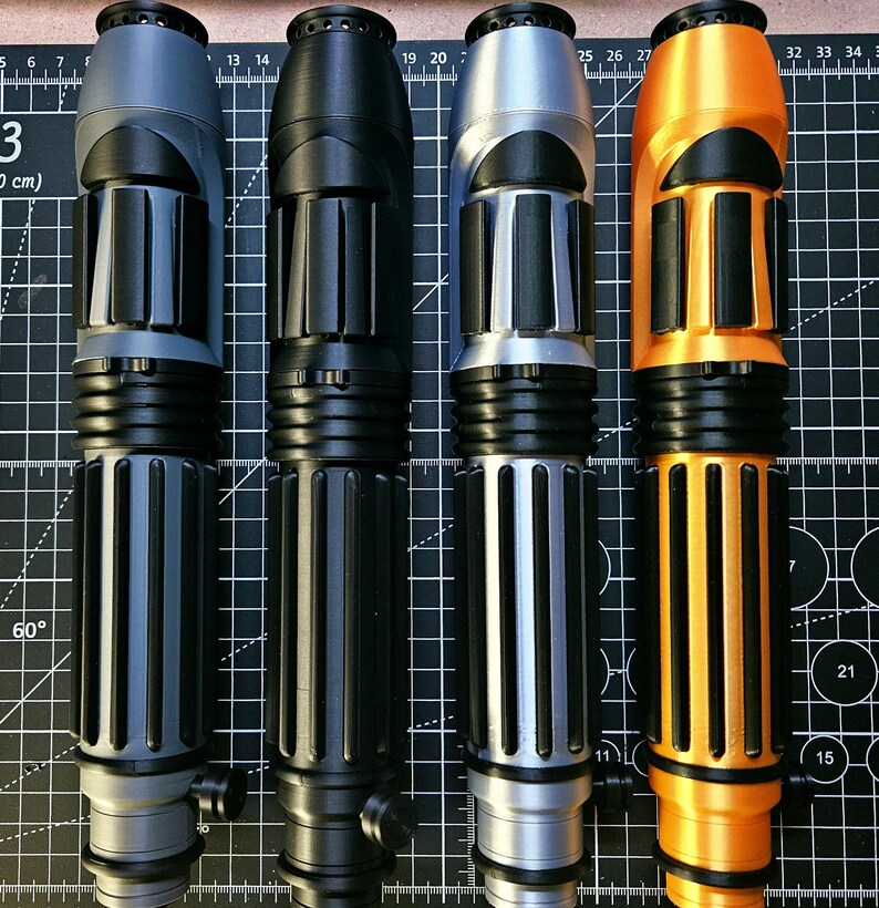 May include: Four cylindrical handles with ribbed textures and black accents, arranged vertically. The handles are coloured matte grey, solid black, metallic silver, and bright orange. Each features a circular top cap and a small side knob.