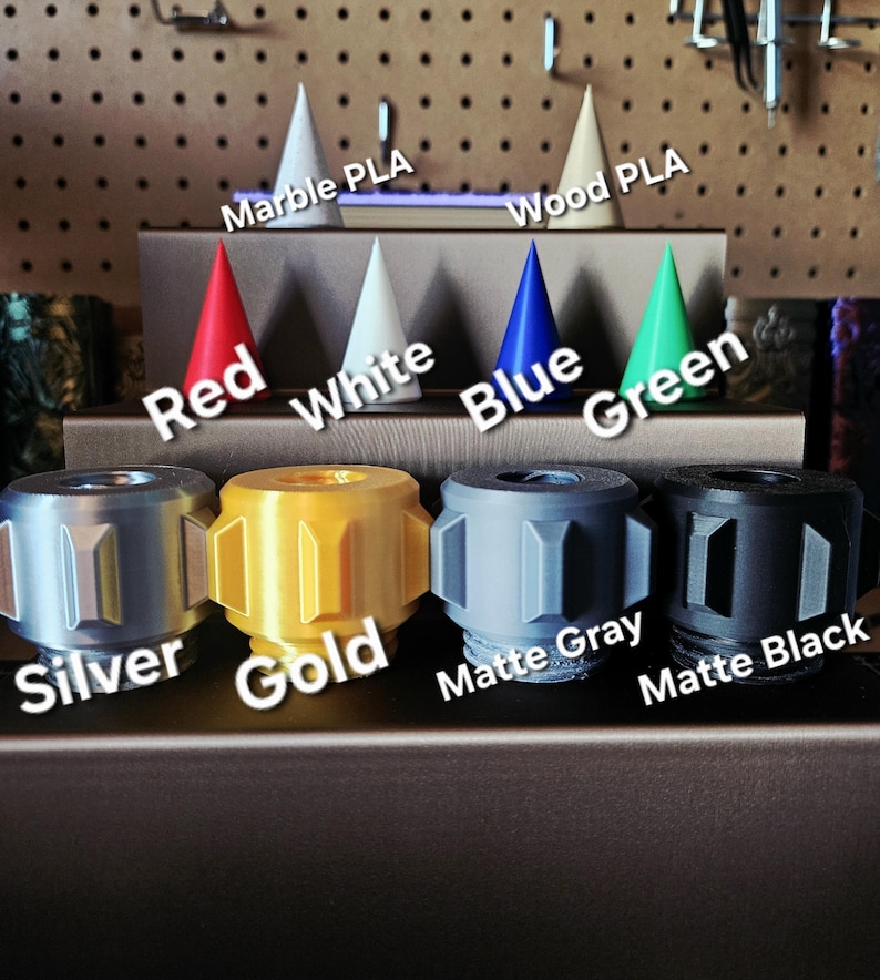 Puede incluir: Una exhibici&oacute;n de objetos impresos en 3D en varios colores y materiales. La imagen muestra varios objetos cil&iacute;ndricos en plata, oro, gris mate y negro mate, junto con objetos en forma de cono en rojo, blanco, azul y verde. Las etiquetas de texto identifican los colores y materiales.