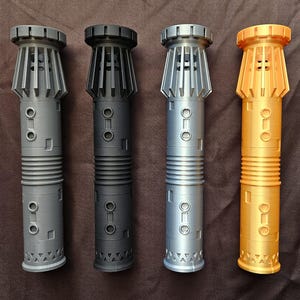 Pu&ograve; includere: Quattro repliche di spade laser in grigio, nero, argento e oro. Ognuna ha un corpo cilindrico con un'impugnatura a coste, dettagli rettangolari e circolari e una parte superiore svasata con lamelle verticali. La spada laser dorata ha un design superiore leggermente diverso.