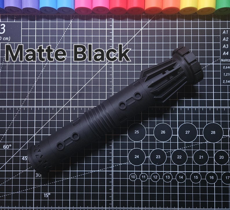 Pu&ograve; includere: Un oggetto cilindrico nero opaco con una superficie strutturata, con dettagli circolari e rettangolari. Il testo "Matte Black" &egrave; visualizzato sopra l'oggetto. Lo sfondo &egrave; un tappetino da taglio nero con linee di griglia e segni di misurazione.