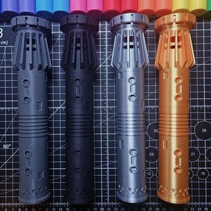 Pu&ograve; includere: Quattro elsi di spada laser stampati in 3D in grigio, nero, argento e oro. Ogni elsa presenta un design dettagliato con sezioni a coste, accenti circolari e una base geometrica. Su un tappetino da taglio nero con misure metriche.