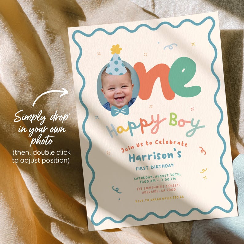 May include: A personalized first birthday invitation with a photo of a baby wearing a party hat and bow tie. The invitation features the words "Happy Boy" and event details in colorful, playful fonts. The invitation is on a cream background with a blue border.