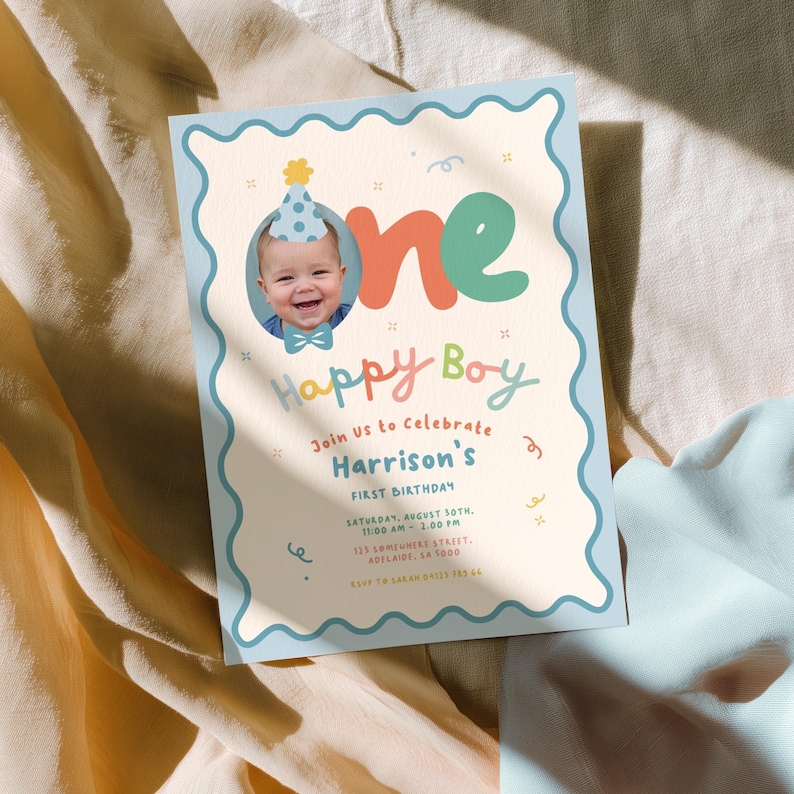 May include: A light blue and cream-colored first birthday invitation. The invitation features a photo of a baby wearing a party hat, the words "one Happy Boy", and event details. The invitation has a wavy border.