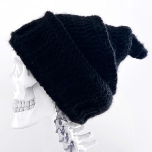 May include: A black knitted beanie with a pointed top. The beanie is worn on a white plastic skull.