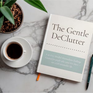 May include: A white book titled "The Gentle DeClutter" with a teal accent, a cup of coffee, a pen, and a potted plant on a marble surface. The book's subtitle reads "A 30-Day Mindful Minimalism Challenge."
