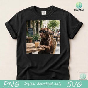 May include: A black short-sleeved t-shirt featuring a central graphic print of a brown Labrador dog wearing black sunglasses, sitting at a wooden cafe table and drinking from a clear plastic cup with a straw. The text Coffee Good Days & Labs is visible.