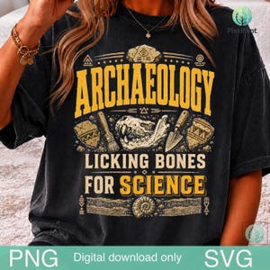 May include: A black t-shirt featuring a yellow graphic with the text ARCHAEOLOGY LICKING BONES FOR SCIENCE. The design includes illustrations of a skull, a brush, a trowel, pottery shards, and an ammonite fossil arranged in a central composition.