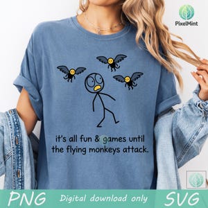 May include: Blue t-shirt with a humorous graphic of a stick figure being attacked by flying monkeys. The text reads "it's all fun & games until the flying monkeys attack."