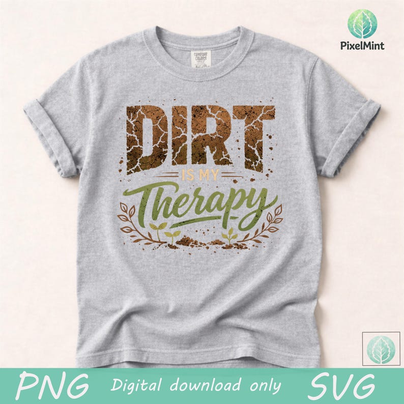 Puede incluir: Una camiseta gris claro con las mangas enrolladas. La camiseta presenta el texto "DIRT is my Therapy" en un dise&ntilde;o desgastado y terroso. La palabra "DIRT" es marr&oacute;n, y "Therapy" es verde con un borde floral.