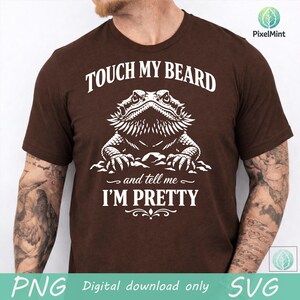 May include: A brown t-shirt with the text "TOUCH MY BEARD" above a detailed white illustration of a bearded dragon. Below the illustration, the text reads "and tell me I'M PRETTY".