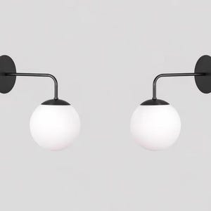 Set di 2 applique da parete in stile Mid-Century Modern con globo in vetro opalino e braccio in metallo nero, ideali per camera da letto e corridoio.