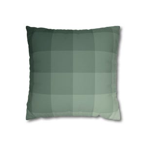 May include: Square decorative pillow with a green plaid pattern. The pillow features a gradient of green shades, creating a subtle checkered design. The pillow is a square shape and appears soft and comfortable.