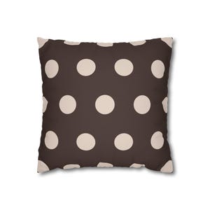 Pode incluir: Almofada quadrada com fundo castanho e grandes bolinhas creme espaçadas uniformemente. O design oferece uma estética simples, mas elegante, ideal para decoração de interiores.