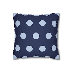 Pode incluir: Almofada quadrada com fundo azul marinho e grandes bolinhas azuis claras. A almofada tem um design simples e limpo, adequado para adicionar um toque de padrão a um sofá ou cama.