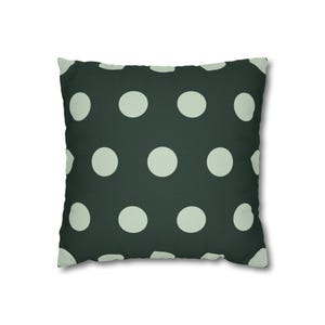 Pode incluir: Almofada quadrada com fundo verde escuro e grandes bolinhas verde claro espaçadas uniformemente. A parte de trás da almofada é de cor lisa. Um item decorativo para a casa.