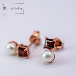 Könnte beinhalten: Ohrringe aus Roségold mit einem quadratischen, tiefroten Edelstein und einer weißen Perle. Die Ohrringe sind von Perlae Atelier. Das Design hat einen Steckerverschluss. Die Edelsteine sind quadratisch geschliffen.