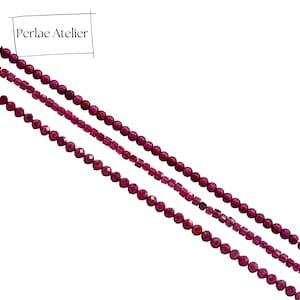 Peut inclure: Quatre rangées de perles de pierres précieuses rouge foncé de formes et tailles variées. Les perles comprennent des formes rondes, facettées et rectangulaires. Le coin supérieur gauche de l'image porte le texte "Perlae Atelier" dans un encadré noir.