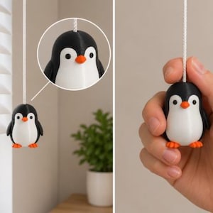 May include: A penguin-shaped blind pull cord handle featuring a black and white body with a small orange beak and orange feet. The figure is attached to a white cord, shown both hanging from a window blind and held in a hand for scale.
