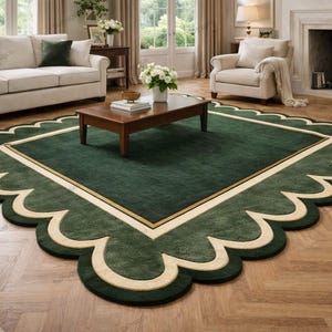 Pode incluir: Um tapete quadrado grande com um campo central verde-floresta profundo, contornado por uma linha dourada fina e uma borda larga e recortada na cor creme. O tapete tem uma textura macia e uniforme sobre um piso de madeira clara.