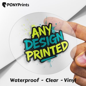 Puede incluir: Una pegatina de vinilo transparente con el texto "ANY DESIGN PRINTED" en verde azulado y amarillo. La pegatina tiene un contorno negro y se muestra con una mano. Las palabras "Waterproof - Clear - Vinyl" están impresas en la parte inferior.