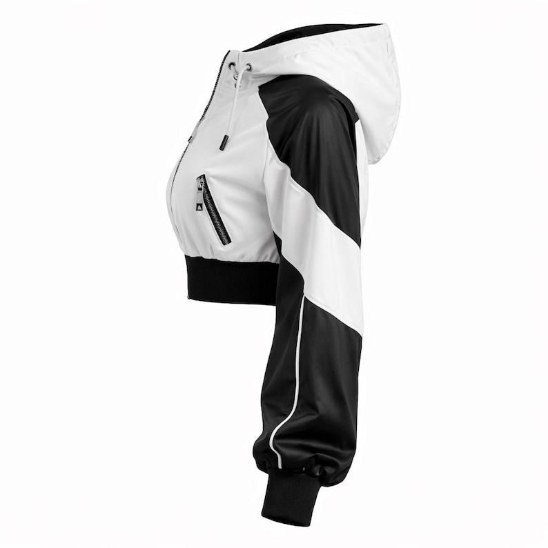 May include: Cropped white and black jacket with a hood. The jacket features a white body with black accents on the sleeves and sides. It has a zipper closure and black ribbed cuffs and hem. The jacket is designed with a sporty aesthetic.