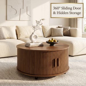 May include: A round, dark wood coffee table with vertical slatted sides, two small rectangular handles, and a 360-degree sliding door mechanism for hidden storage. The table surface holds a white ceramic vase and a dark bowl with three pears.