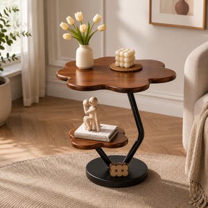 May include: A two-tiered side table with a dark wood finish and a flower-shaped top and lower shelf. The table features a black metal frame with a curved support and a circular base. A small decorative wooden figure sits on the lower shelf.