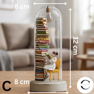 May include: A decorative glass cloche containing a tall stack of multicolored books and a figurine sitting on a yellow chair reading a book. A lightbulb hangs from the top inside. The base is white, and the dimensions are 8 cm by 12 cm.