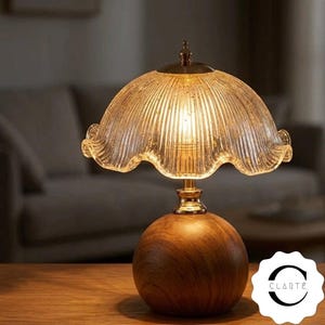 May include: A table lamp featuring a spherical wooden base with a natural grain pattern and a fluted, scalloped glass shade. The lamp emits a warm glow from within the clear, textured glass. A small metallic finial sits atop the shade.