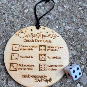May include: A round wooden ornament featuring the laser-engraved text Christmas Drunk Dice Game with instructions for each die roll outcome and a white six-sided die with black pips. A black cord is attached to the top for hanging purposes.