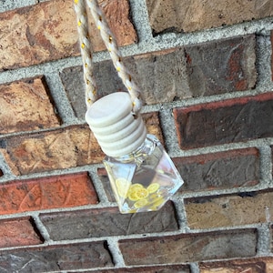 May include: A clear, faceted glass car air freshener with a wooden cap and a decorative rope. The air freshener contains yellow lemon slices. The background is a brick wall.