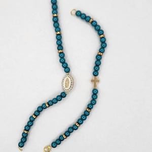 May include: Two rosaries with teal beads and gold-colored accents. One rosary features a gold cross and the other has a gold-framed oval pendant with a religious image. Both rosaries have gold clasps.