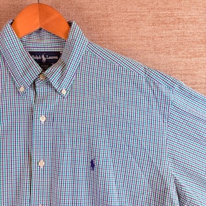 May include: A long-sleeve button-down shirt featuring a small purple and teal gingham check pattern. The shirt includes a button-down collar, a front button placket, and a purple embroidered Ralph Lauren logo on the left side of the chest.