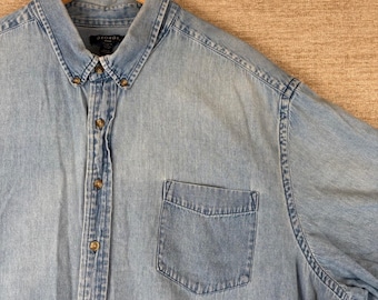 May include: A light blue denim button-down shirt with a pointed collar, a single chest pocket, and brown buttons. The shirt features a George brand label on the inside collar and has visible stitching along the placket, pocket, and shoulder seams.