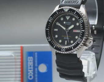 May include: A Seiko Quartz Professional 200m dive watch with a black dial, luminous hands and markers, and a black rotating bezel. The watch has a black rubber strap and a stainless steel case. The watch is displayed on a clear stand.
