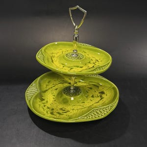 May include: Two-tiered serving tray with a silver handle and stem. The trays are a vibrant green with a speckled pattern and decorative edges. A decorative piece for serving appetizers or desserts.