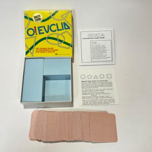 May include: A yellow O! EUCLID card game box with geometric line art, an open box base with light blue dividers, two white instruction sheets with black text and shape diagrams, and a stack of cards with a red and white patterned back.