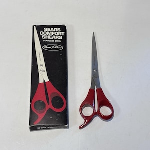 Könnte beinhalten: Ein Paar Sears Comfort Shears mit roten Griffen und Edelstahlklingen, neben der Originalverpackung. Die Schachtel zeigt weißen Text und eine rot-weiße Abbildung der Schere. Der Text auf der Schachtel lautet "Sears Comfort Shears Stainless Steel".