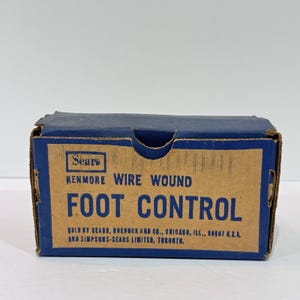 Puede incluir: Una caja vintage de Kenmore Foot Control. La caja es azul y marrón con el logotipo de Sears y el texto "KENMORE WIRE WOUND FOOT CONTROL". La caja está hecha de cartón y tiene forma rectangular.