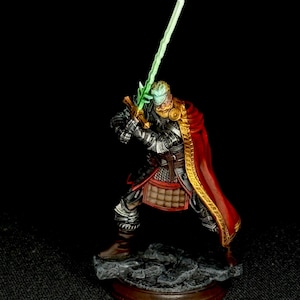 May include: A miniature figurine of a warrior in silver plate armor and a red cloak with gold trim, holding a glowing green sword aloft. The figure has blonde hair, a beard, and stands on a textured gray stone base with a circular brown border.