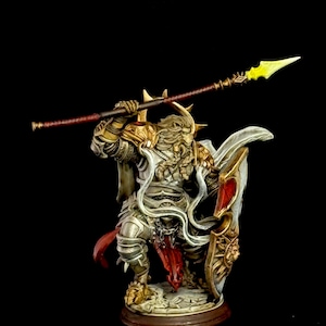 Può includere: Statuetta in miniatura dettagliata di un guerriero in armatura ornata, con una lancia e uno scudo. La figura è prevalentemente argentata e dorata, con un mantello bianco e dettagli rossi. La lancia ha una lama gialla.