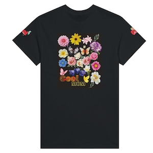 Può includere: T-shirt nero con un design floreale con vari fiori, farfalle e la scritta "Cool Mom" in un carattere colorato e strutturato. La maglietta ha maniche corte.